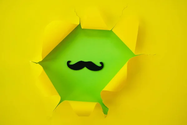 Papel amarillo rasgado sobre un fondo verde con bigote . — Foto de Stock