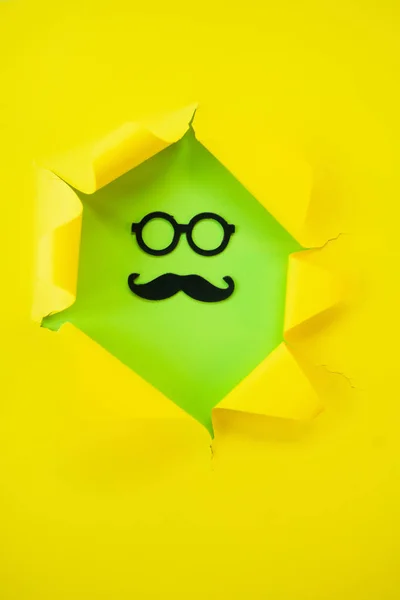 Papel amarillo rasgado sobre un fondo verde con bigote y vidrio — Foto de Stock