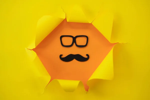 Papel amarillo desgarrado sobre un fondo naranja con bigote y vidrio — Foto de Stock