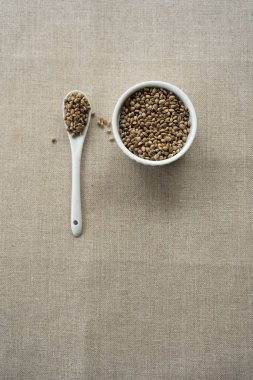 Keten arka plan üzerinde kenevir tohumu dolu beyaz bir seramik kase