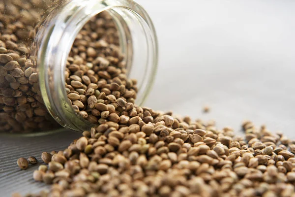 Keten arka planda kenevir tohumu ile devrilmiş cam kavanoz