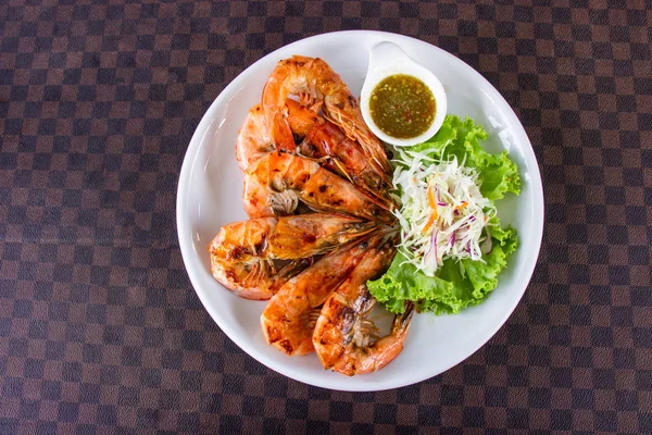 Crevettes grillées aux fruits de mer décorées de légumes et sauce piquante piquante trempette dans un plat en céramique blanche mettre sur le sol en cuir le motif de grille . — Photo
