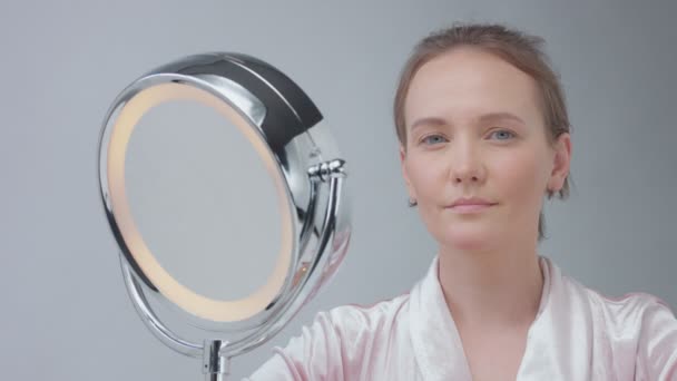 Caucasian woman with mirror with ring light with no makeup look examine her skin and makes facial treatment Stock Video