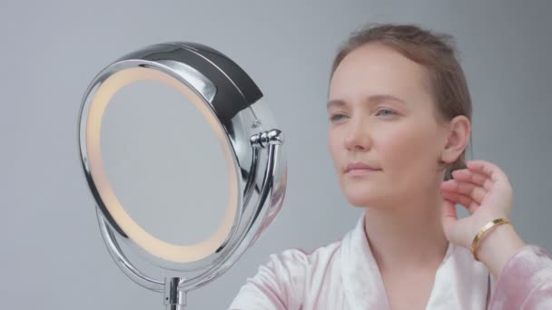Kaukasische vrouw met de spiegel met ring licht met geen make-up look onderzoeken van haar huid en maakt gezichtsbehandeling — Stockvideo