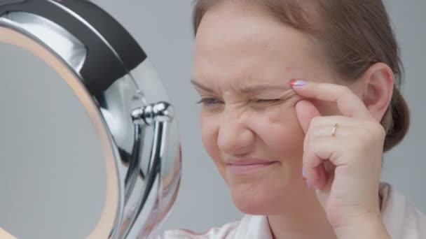 Белая женщина с зеркалом с кольцом света без макияжа взгляд изучить ее кожу и делает уход за лицом — стоковое видео