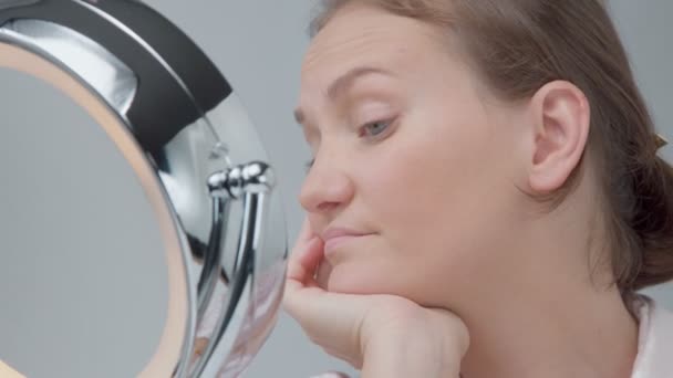 Mujer caucásica con espejo con anillo de luz sin maquillaje mirada examinar su piel y hace tratamiento facial — Vídeo de stock