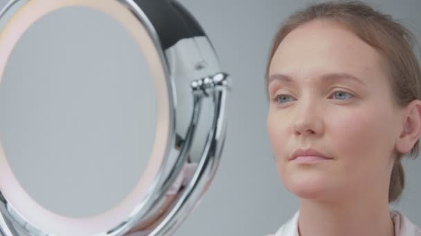 Kaukasische vrouw met de spiegel met ring licht met geen make-up look onderzoeken van haar huid en maakt gezichtsbehandeling — Stockvideo