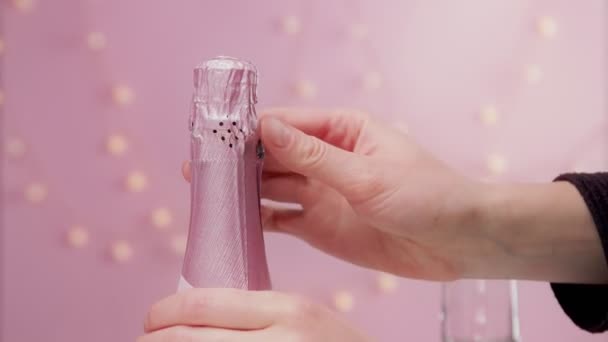 Vino espumoso rosa con mano de mujer y copas sobre fondo rosa con luces navideñas — Vídeos de Stock