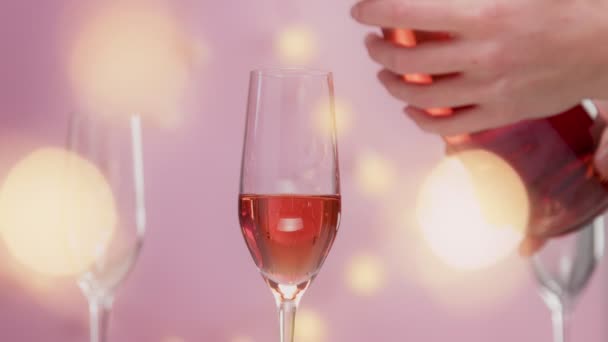 Pink sparkling wine with womans hand and glasses on pink background with christmas lights — Stock Video