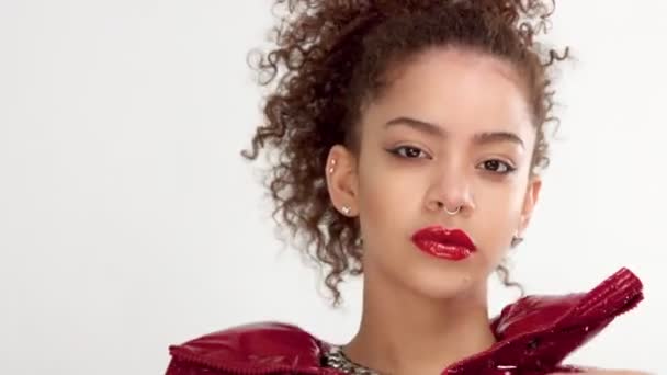 Jeune femme avec des lèvres de laque rouge et veste brillante rouge sur blanc en studio — Video