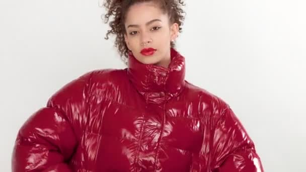 Jonge vrouw met rode lak lippen en rode glanzende jasje op wit in de studio — Stockvideo