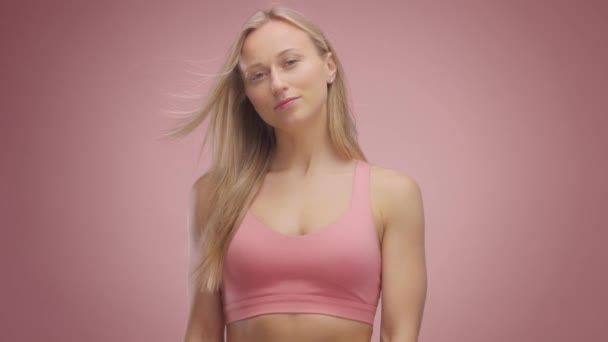 Modelo loira em estúdio sobre fundo rosa com cabelo soprando no ar — Vídeo de Stock