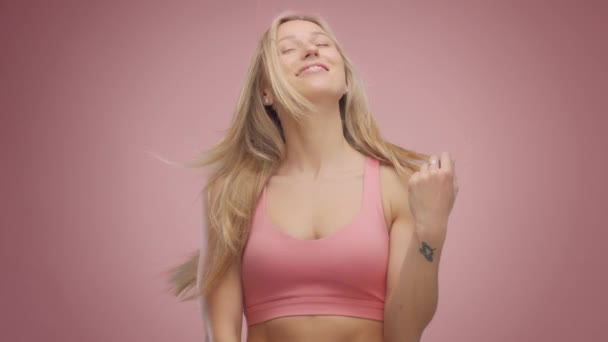 金发模型在工作室在粉红色的背景与头发吹在空气中 — 图库视频影像