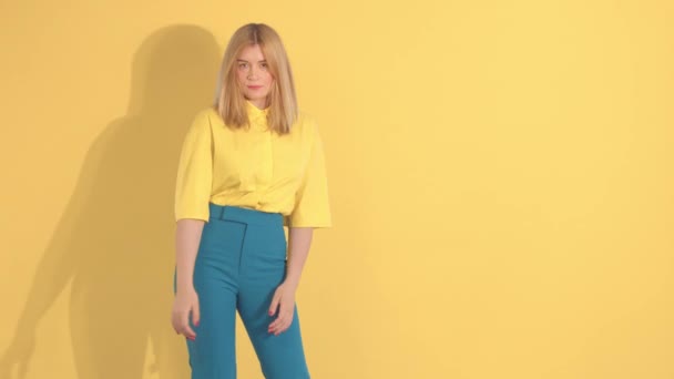 Mladá žena v jasných šatech na jasně žlutém pozadí ve studiu — Stock video