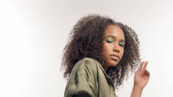 Modelo de raza mixta joven en estudio en blanco con pelo rizado, maquillaje de ojos verde brillante — Vídeos de Stock