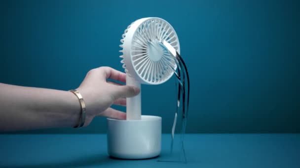 Liten vit ventilator med silverremsor blåsning slås på av kvinnans hand — Stockvideo