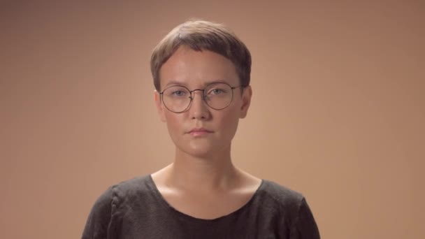 Mujer caucásica con corte de pelo corto lleva gafas en el estudio sobre fondo beige — Vídeo de stock