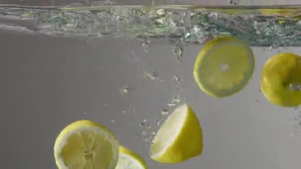 Limoni tagliati immersi nell'acquario trasparente con acqua su fondo grigio — Video Stock