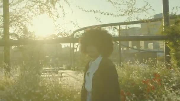 Portrait of mixed race black woman in the park full of flowers. Laughing in contour sunlight — Stock Video