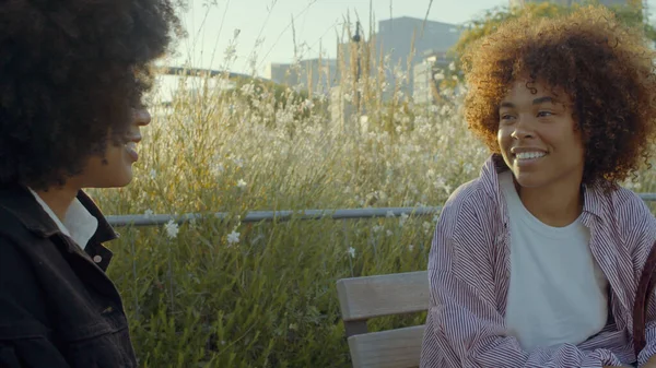 Un couple de femmes noires métissées parlant dans le parc entouré de fleurs au soleil du matin — Photo