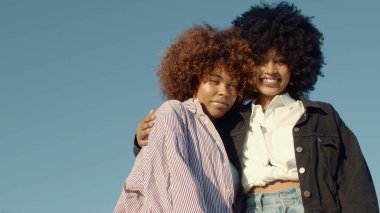 İki melez ırk siyahi kadın açık havada birbirine sarılıyor. İki melez kadın, uzun saçlı.