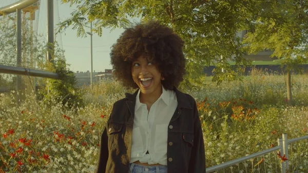 Retrato de mujer negra de raza mixta en el parque lleno de flores. Riendo en el contorno de la luz del sol —  Fotos de Stock