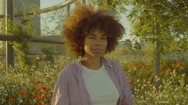 Ritratto di donna nera di razza mista nel parco pieno di fiori con enormi capelli afro — Foto Stock