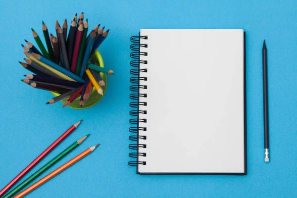 蓝色桌子上有白色页面和五颜六色的信纸的空螺旋笔记本 在彩色背景上带有记事本的工作场所 用于输入文本的草绘簿 顶部视图 回到学校的概念 — 图库照片