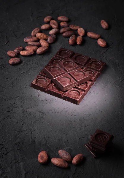 chopped chocolate tablet and cocoa beans on rough gray background