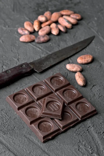 split chocolate tablet and group of cocoa beans on rustic black textured background