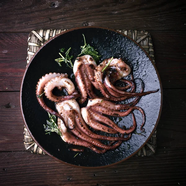 Octopus cooked with parsley and oil in a porcelain dish on rustic wood