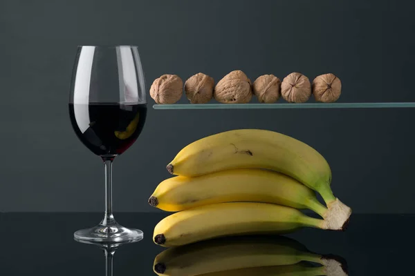 bananas and nuts with glass of wine on dark glass stage