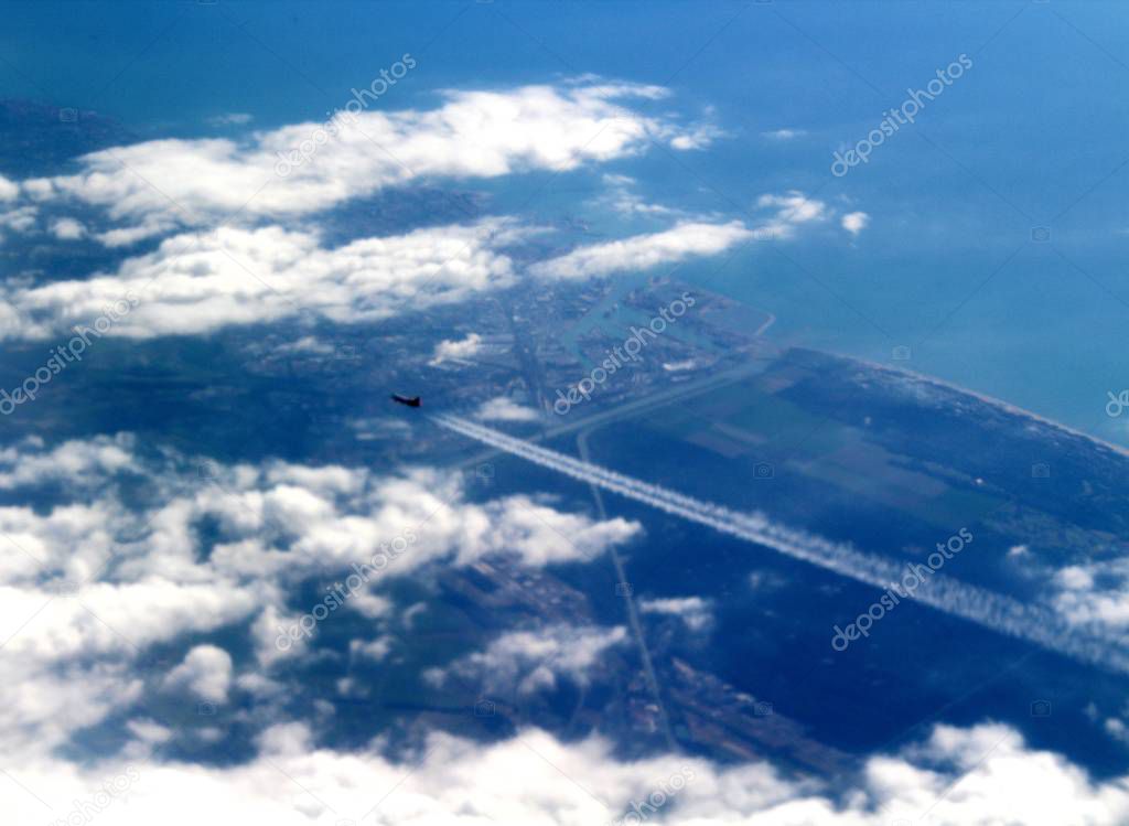 evocative image of military jet flying in the clouds with landscape in the background