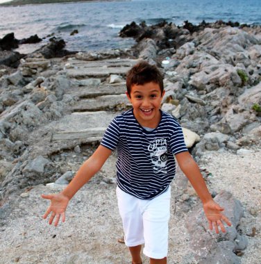 gün batımında deniz tarafından mutlu oynayan çizgili gömlek ve beyaz şort çocuk çağrıştıran görüntü