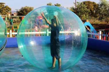 Havuzda yüzen şişme topun içinde eğlenen çocuk görüntüsü.