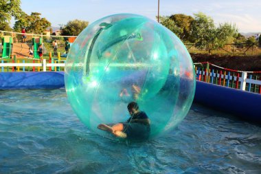 Havuzda yüzen şişme topun içinde eğlenen çocuk görüntüsü.