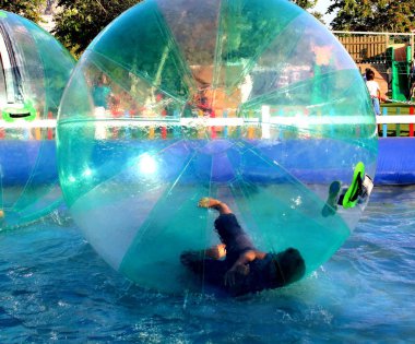 Havuzda yüzen şişme topun içinde eğlenen çocuk görüntüsü.