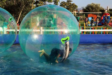 Havuzda yüzen şişme topun içinde eğlenen çocuk görüntüsü.