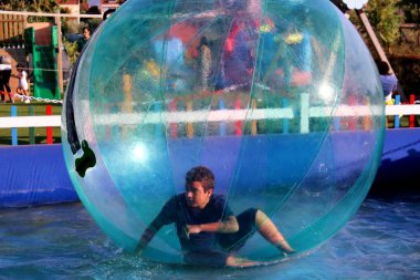 Havuzda yüzen şişme topun içinde eğlenen çocuk görüntüsü.
