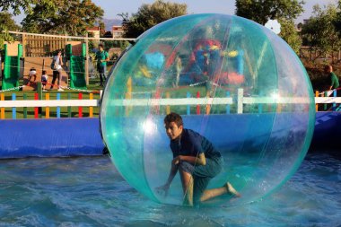 Havuzda yüzen şişme topun içinde eğlenen çocuk görüntüsü.