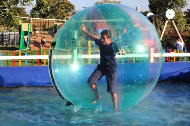 Havuzda yüzen şişme topun içinde eğlenen çocuk görüntüsü.