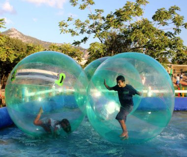 Havuzda yüzen şişme topun içinde eğlenen çocuk görüntüsü.