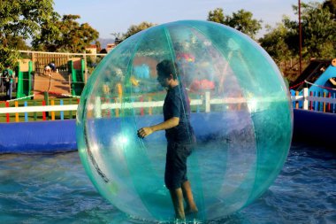 Havuzda yüzen şişme topun içinde eğlenen çocuk görüntüsü.