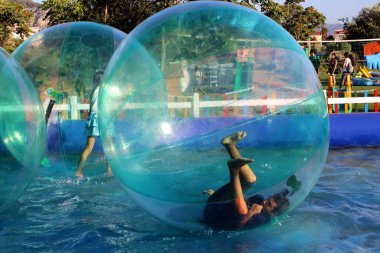 Havuzda yüzen şişme topun içinde eğlenen çocuk görüntüsü.
