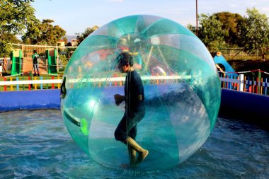 Havuzda yüzen şişme topun içinde eğlenen çocuk görüntüsü.
