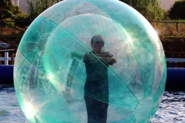 Havuzda yüzen şişme topun içinde eğlenen çocuk görüntüsü.