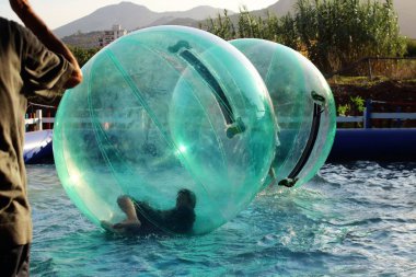 Havuzda yüzen şişme topun içinde eğlenen çocuk görüntüsü.