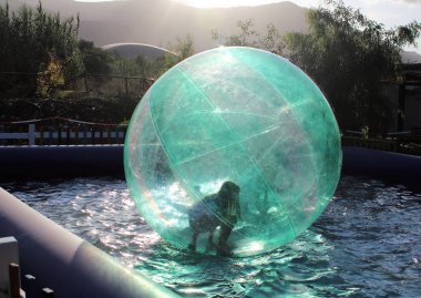 Havuzda yüzen şişme topun içinde eğlenen çocuk görüntüsü.