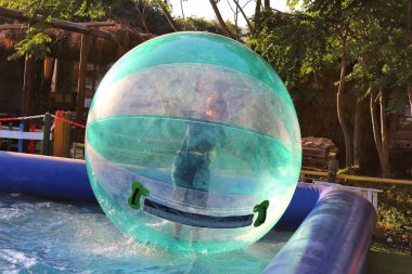 Havuzda yüzen şişme topun içinde eğlenen çocuk görüntüsü.