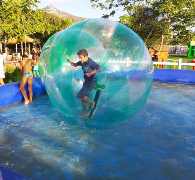 Havuzda yüzen şişme topun içinde eğlenen çocuk görüntüsü.